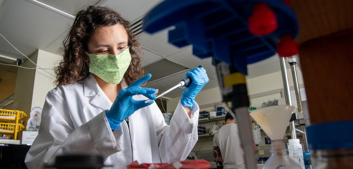 Female student conducts a science experiment in a lab while wearing a face mask